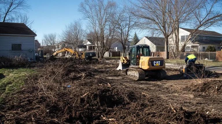 CAT excavator clearing residential lot with debris removal in Johnson City neighborhood development project